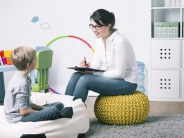 Child therapist writing on clipboard while talking to young child