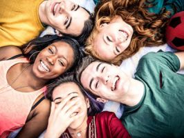 Group of happy teens with colorful t-shirts lying down in a circle smiling and laughing