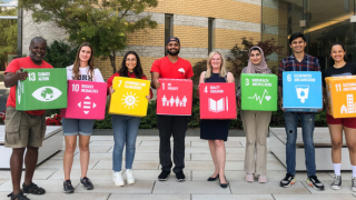 a diverse group of students lined up with President LEnton in the middle holding up UNSDG cubes