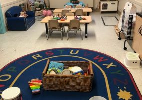 Toddler classroom. Two desks with instruments and toys ontop of a rug that shows the alphabet.
