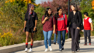 A diverse group of female presenting students walking while smiling at each other on a fall day.