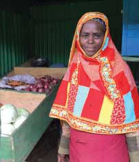 a women stands in front of her vegetable stall